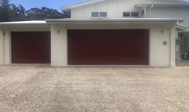 Two timber-look garage doors installed on a light rendered home