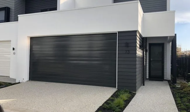 Black slimline sectional garage door installed on a modern white home